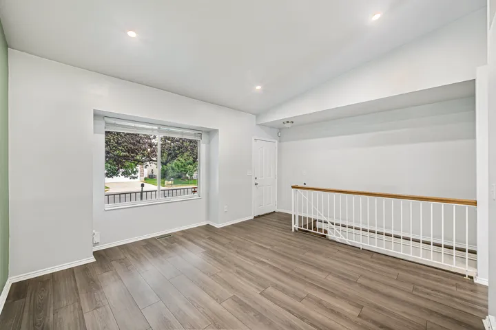 Spacious interior room featuring wood-finish flooring, recessed lighting, and a large picture window with blinds