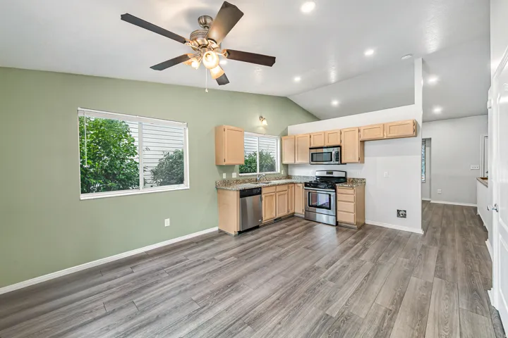 Open-concept kitchen and living area featuring wood-finish flooring, vaulted ceilings with recessed lighting, and a ceiling fan