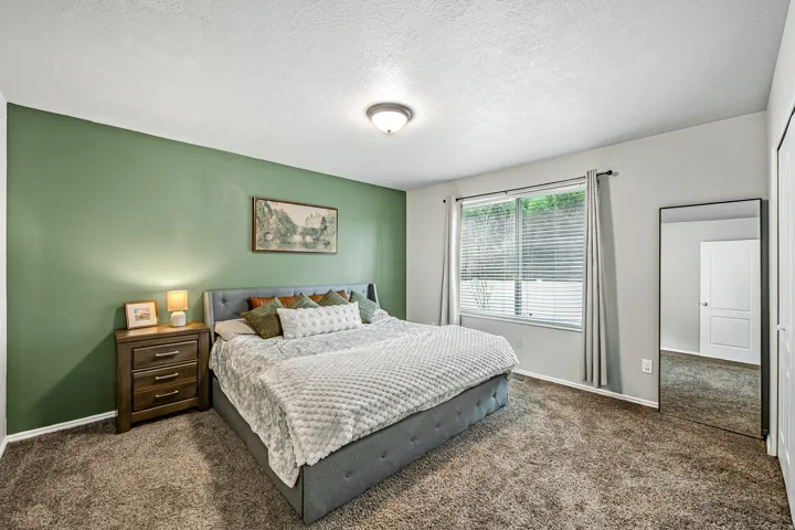 Carpeted bedroom featuring a large window with blinds, a prominent green accent wall, and a ceiling-mounted light fixture