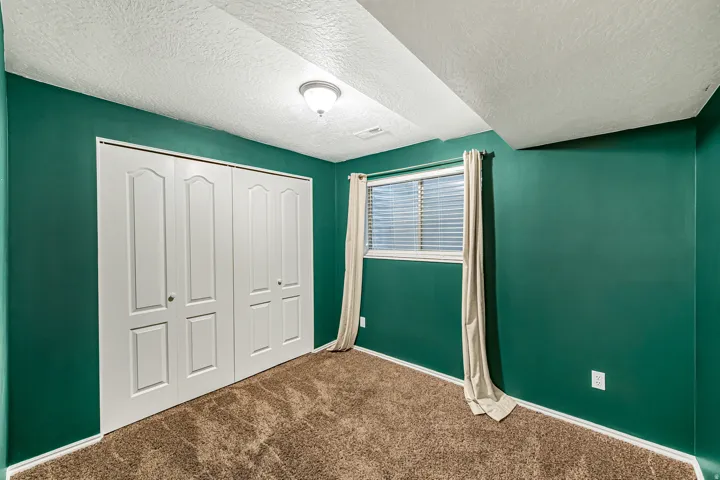 Interior space featuring a window with blinds, bi-fold closet doors, textured ceiling, and a flush mount light fixture