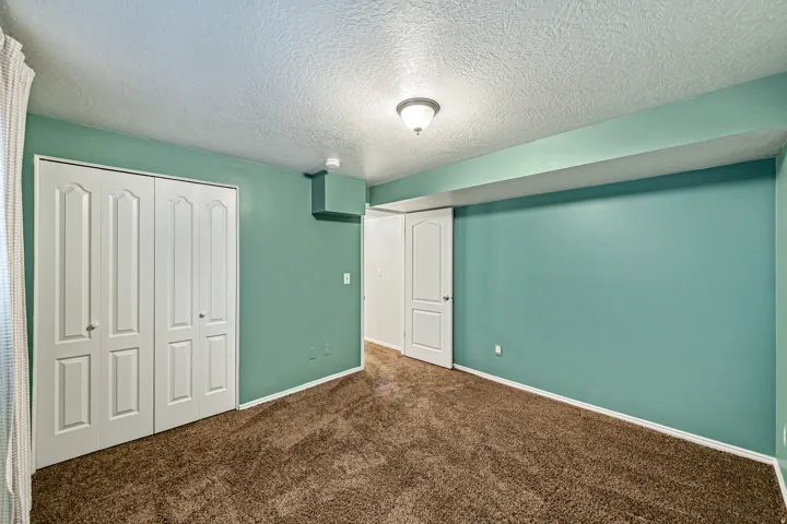Interior room featuring brown carpeting, light teal walls, a white ceiling with textured finish, a ceiling-mounted light fixture, and white bi-fold closet doors