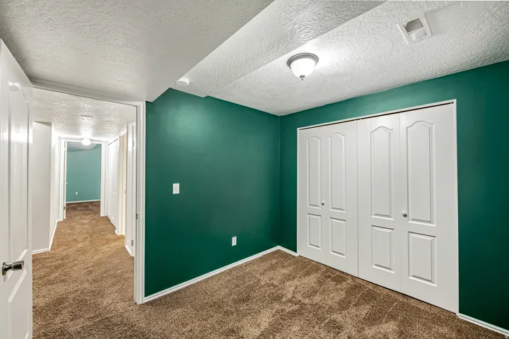 Interior room featuring green walls, textured white ceiling, a ceiling-mounted light fixture, white bi-fold closet doors, and brown carpet flooring