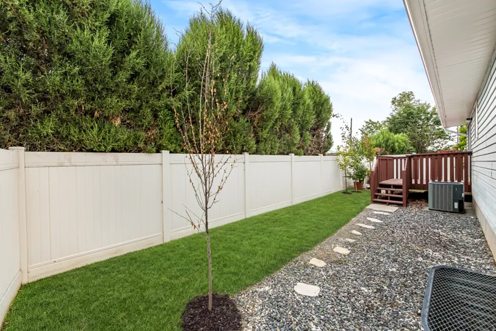 Side yard featuring a vinyl privacy fence, manicured lawn, and a pebble pathway with stepping stones