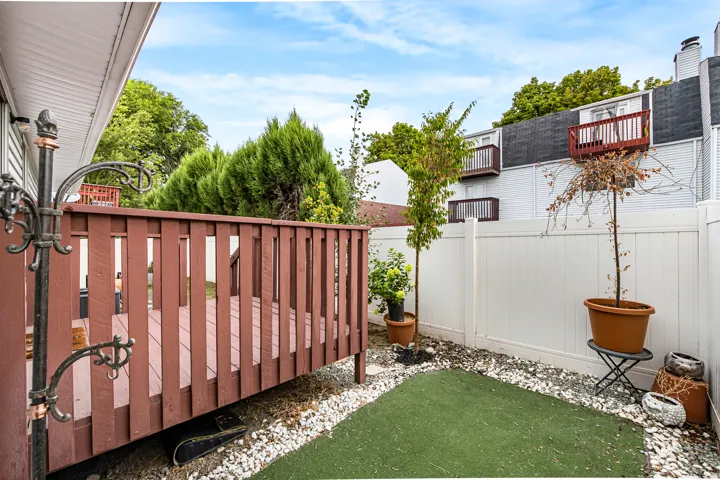 Private outdoor patio featuring a wooden deck and a white privacy fence