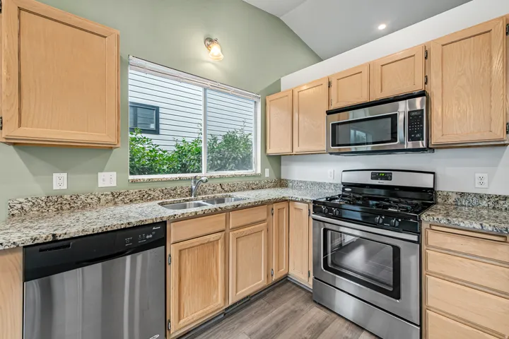Kitchen featuring light wood-finish cabinetry, granite countertops, stainless steel appliances, and a vaulted ceiling