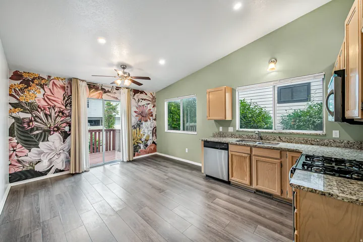 Open-concept living area featuring wood-finish flooring, a vaulted ceiling, and a full-wall floral accent