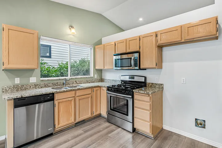Kitchen featuring light wood cabinetry, granite-style countertops, stainless steel appliances, and wood-finish flooring