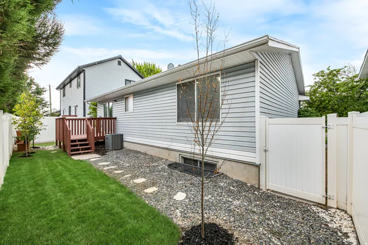 Backyard featuring a wooden deck with railing and stairs, a manicured lawn, gravel landscaping with stepping stones, and white privacy fencing with a gate