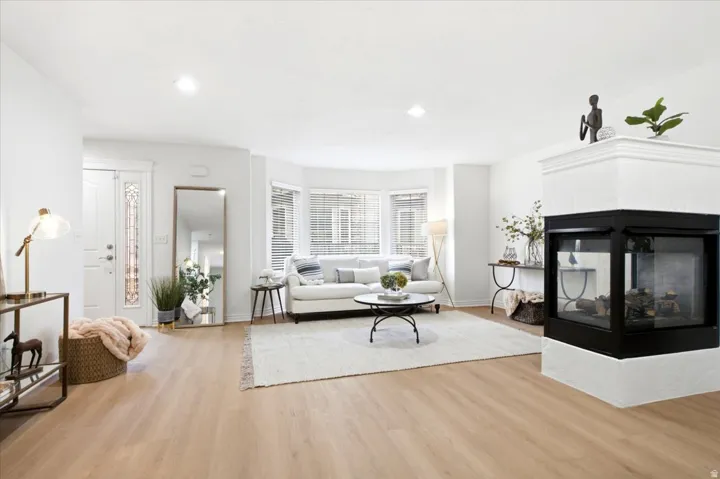 Open-concept living area featuring light wood-finish flooring, a contemporary fireplace with a black glass enclosure, and recessed lighting