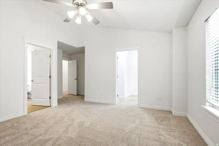 Spacious room featuring vaulted ceilings, neutral-toned carpeting, white trim, and a ceiling fan