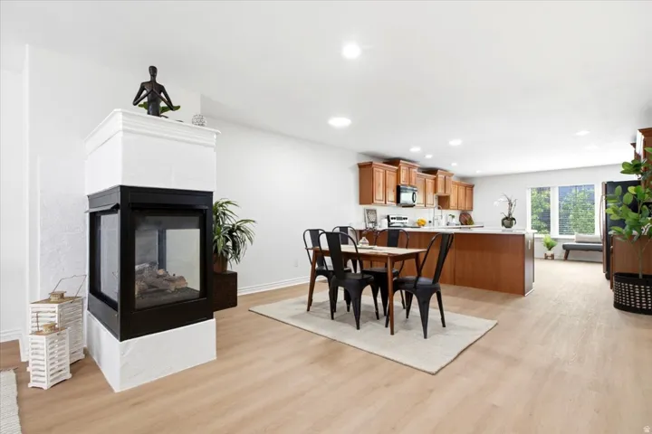 Open-concept living space featuring a modern three-sided fireplace with a white mantel, wood-finish flooring, and recessed ceiling lighting