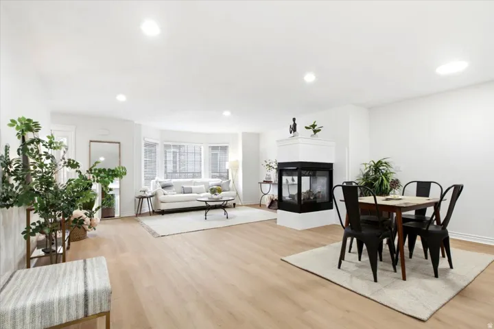 Open-concept living space with light wood-finish flooring, recessed lighting, and a modern two-sided fireplace