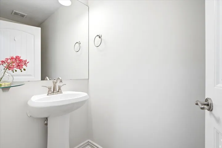 Pedestal sink with brushed nickel faucet, large wall-mounted mirror, and glass shelf