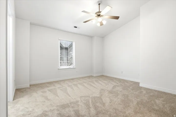 Carpeted room featuring a single window with blinds, a ceiling fan with integrated lighting, and white baseboards