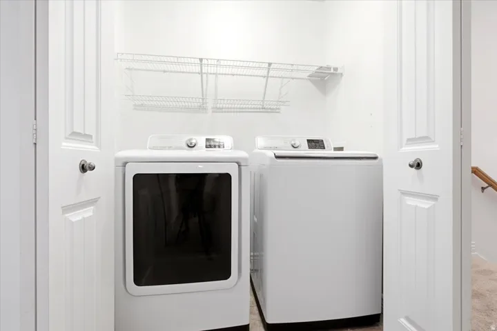 Dedicated laundry area with a white washing machine and dryer, featuring white wire shelving for storage