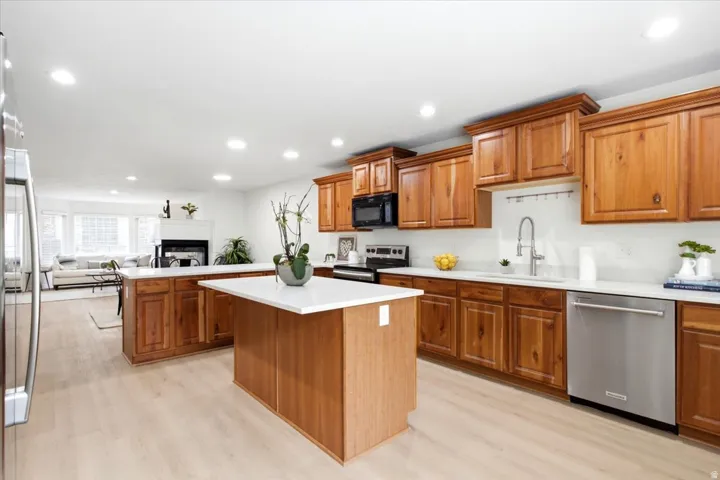 Kitchen featuring warm wood cabinetry, stainless steel appliances, white countertops, a central island, and wood-finish flooring