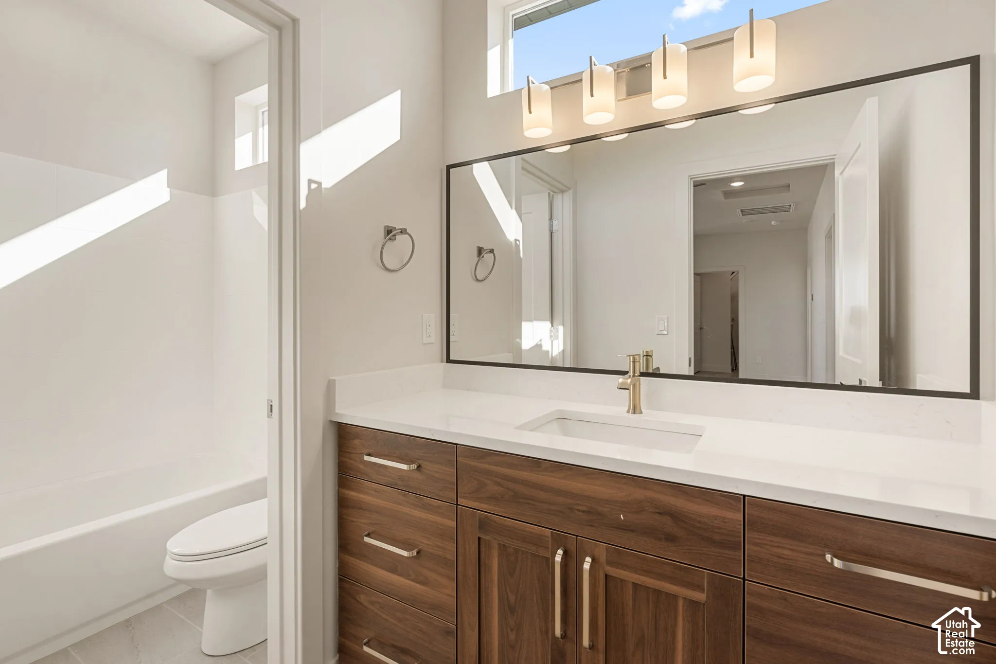 Bathroom vanity featuring a quartz countertop, wood-finish cabinetry, a rectangular undermount sink, a framed mirror, and four-bulb wall-mounted lighting