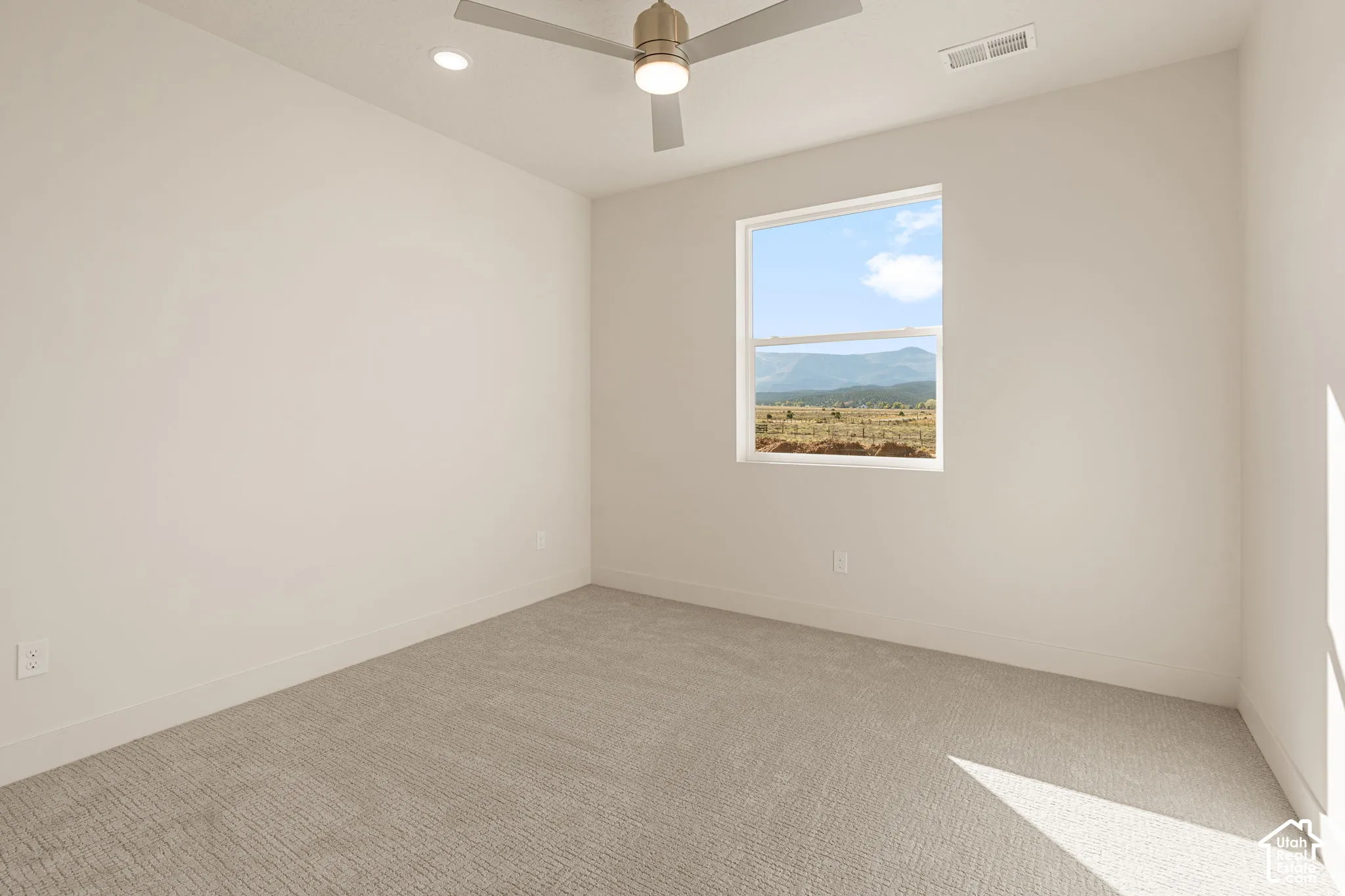 Neutral-toned interior space featuring wall-to-wall carpeting, a multi-blade ceiling fan with integrated lighting, recessed lighting, and a single-pane window showcasing mountain scenery