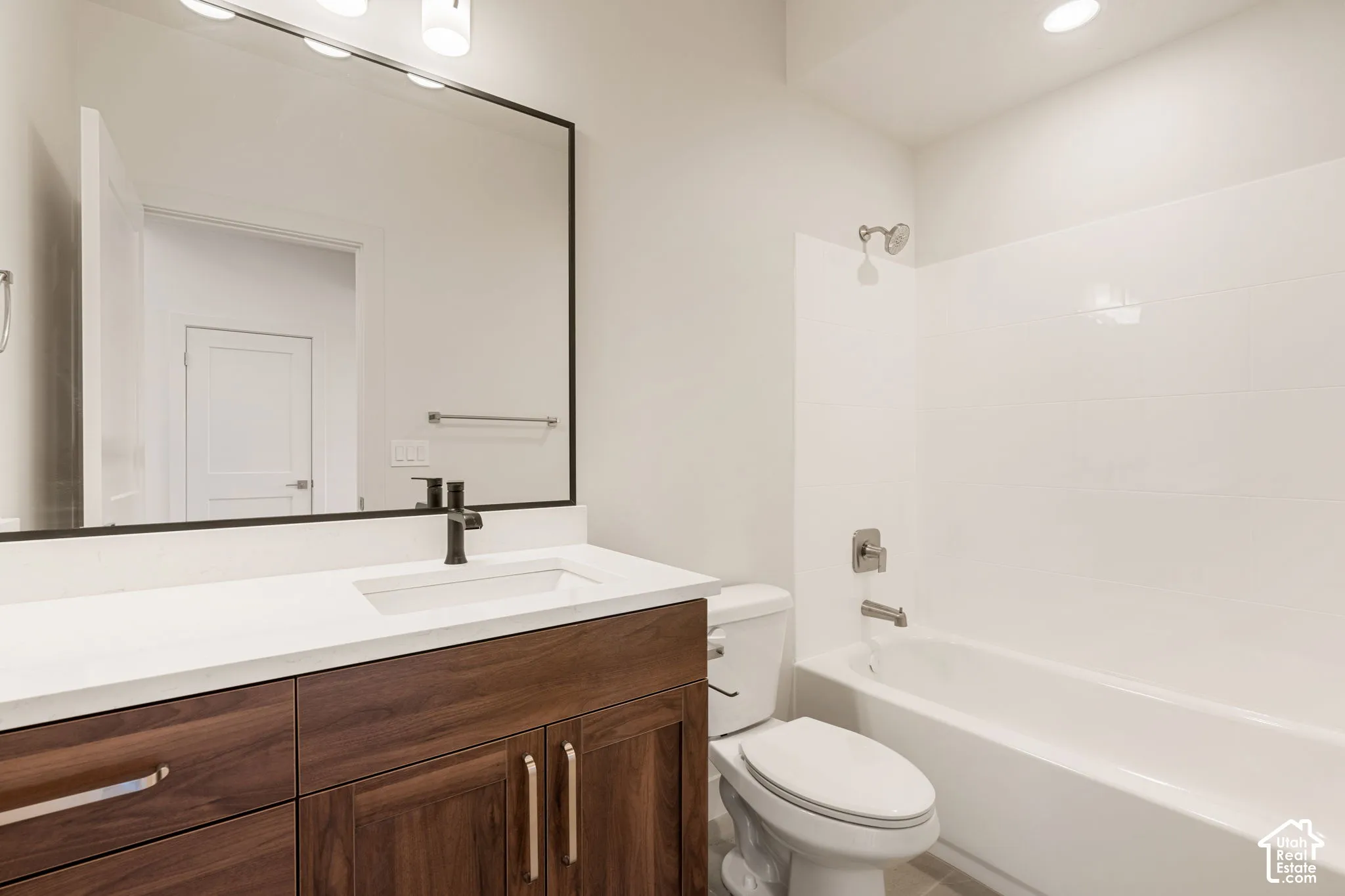 Bathroom featuring a dark wood-finish vanity with a white countertop, rectangular integrated sink, matte black faucet, and a large mirror with a dark metal frame