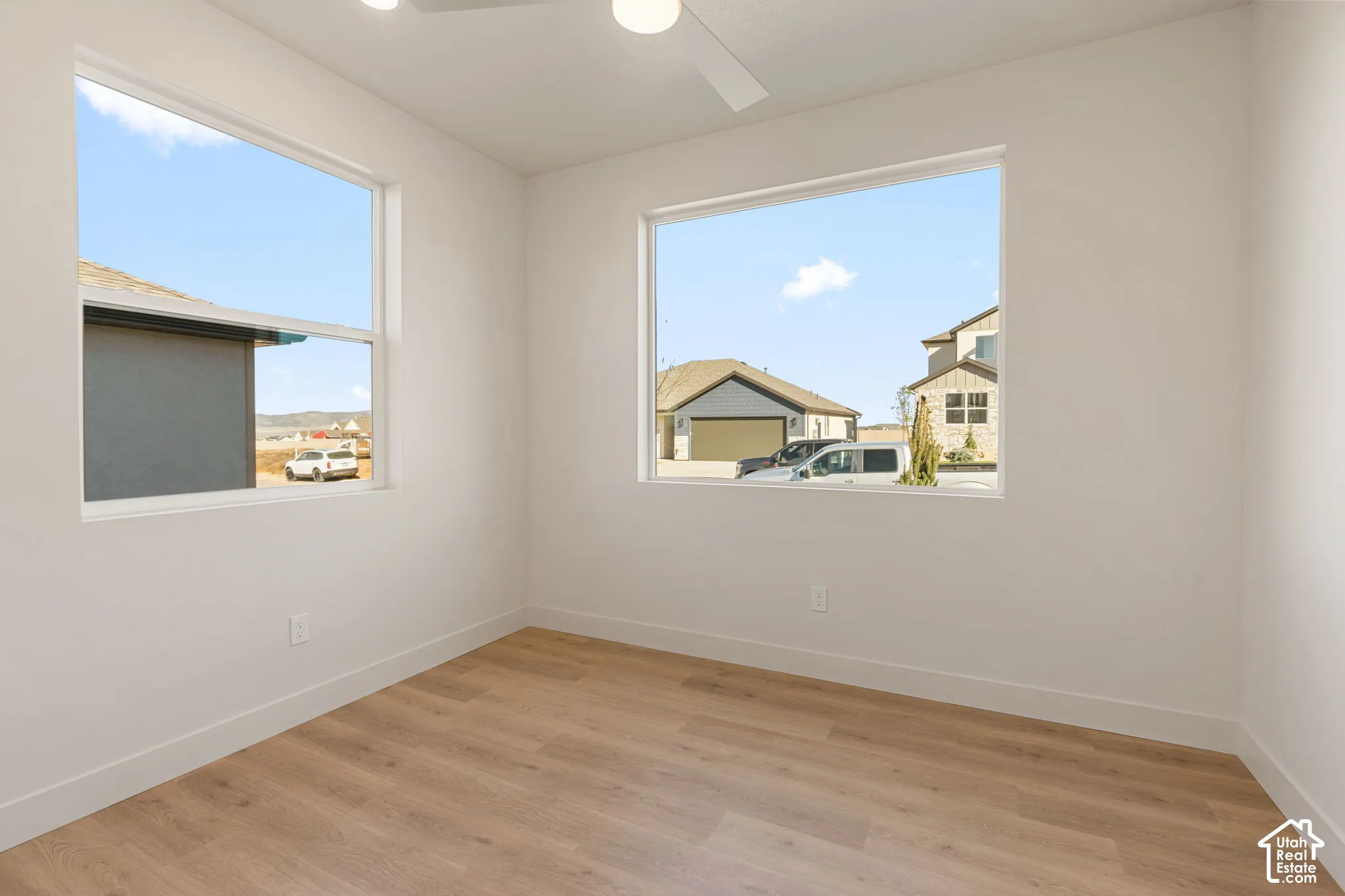 Interior space featuring wood-finish flooring, white walls, dual large-pane windows, and a ceiling-mounted fan with integrated light