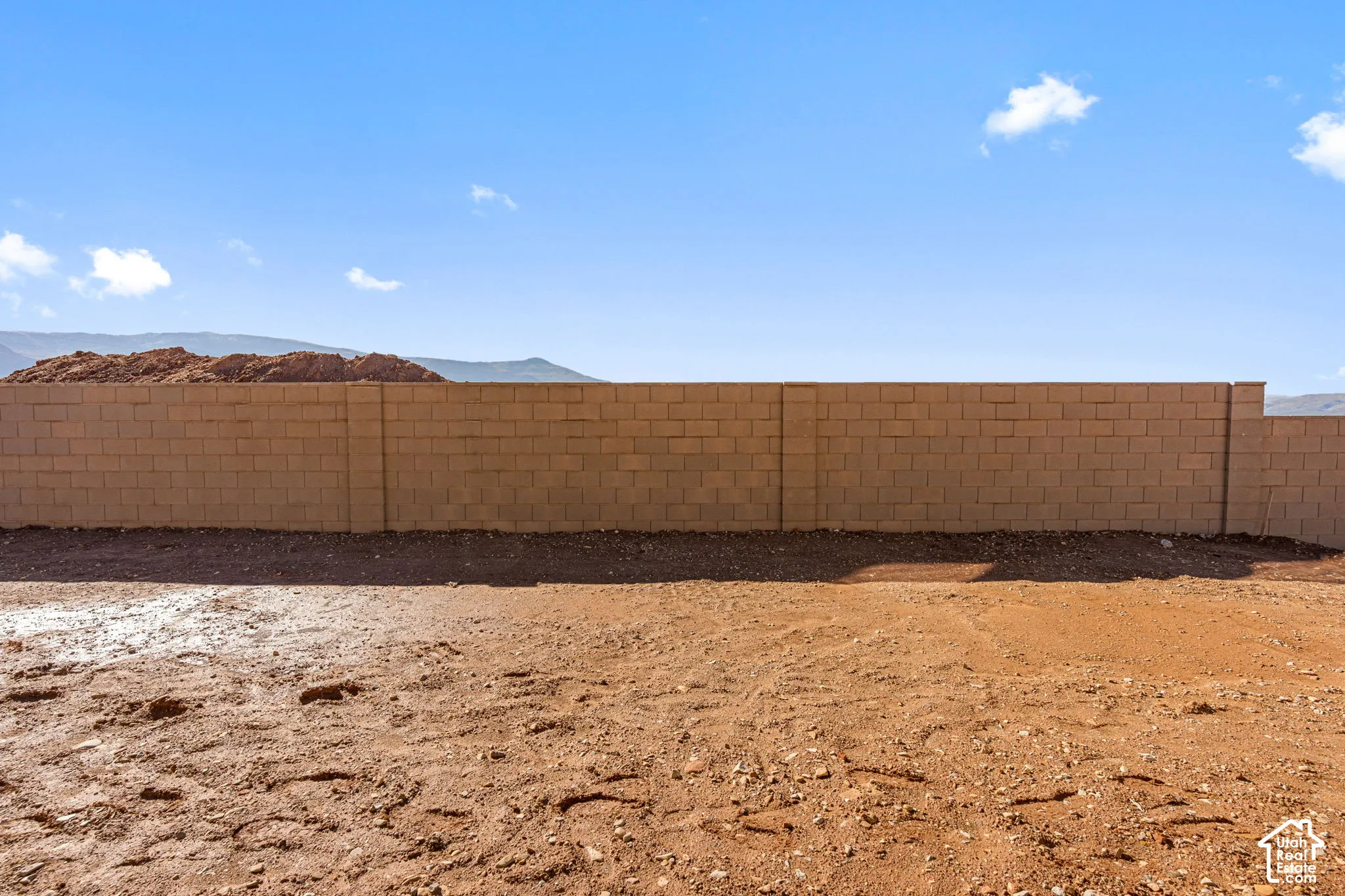 Expansive open lot featuring a concrete block perimeter wall and mountain scenery
