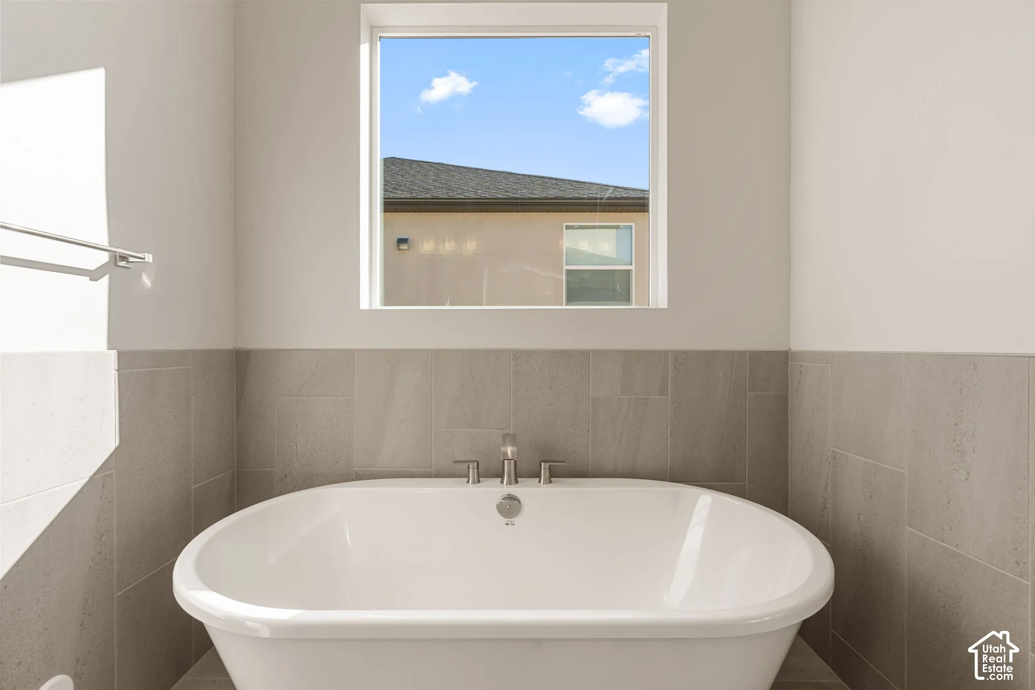 Freestanding soaking tub featuring a chrome faucet, set against tile wall surround and a square picture window