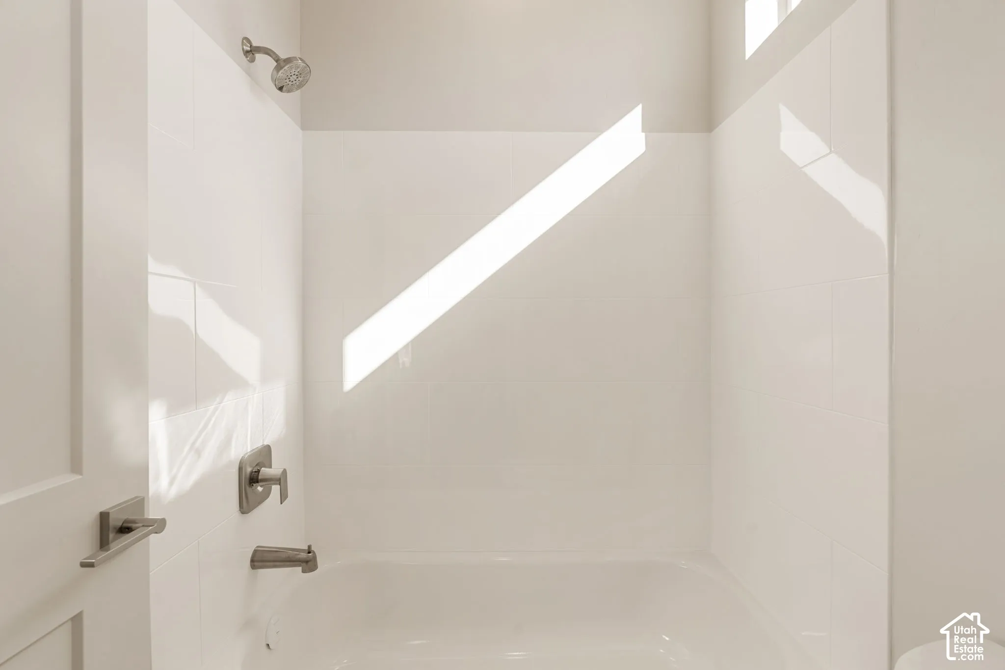 Bathtub enclosure featuring white ceramic wall tile, a brushed metal shower head, a single-handle pressure-balance valve, and a matching tub spout