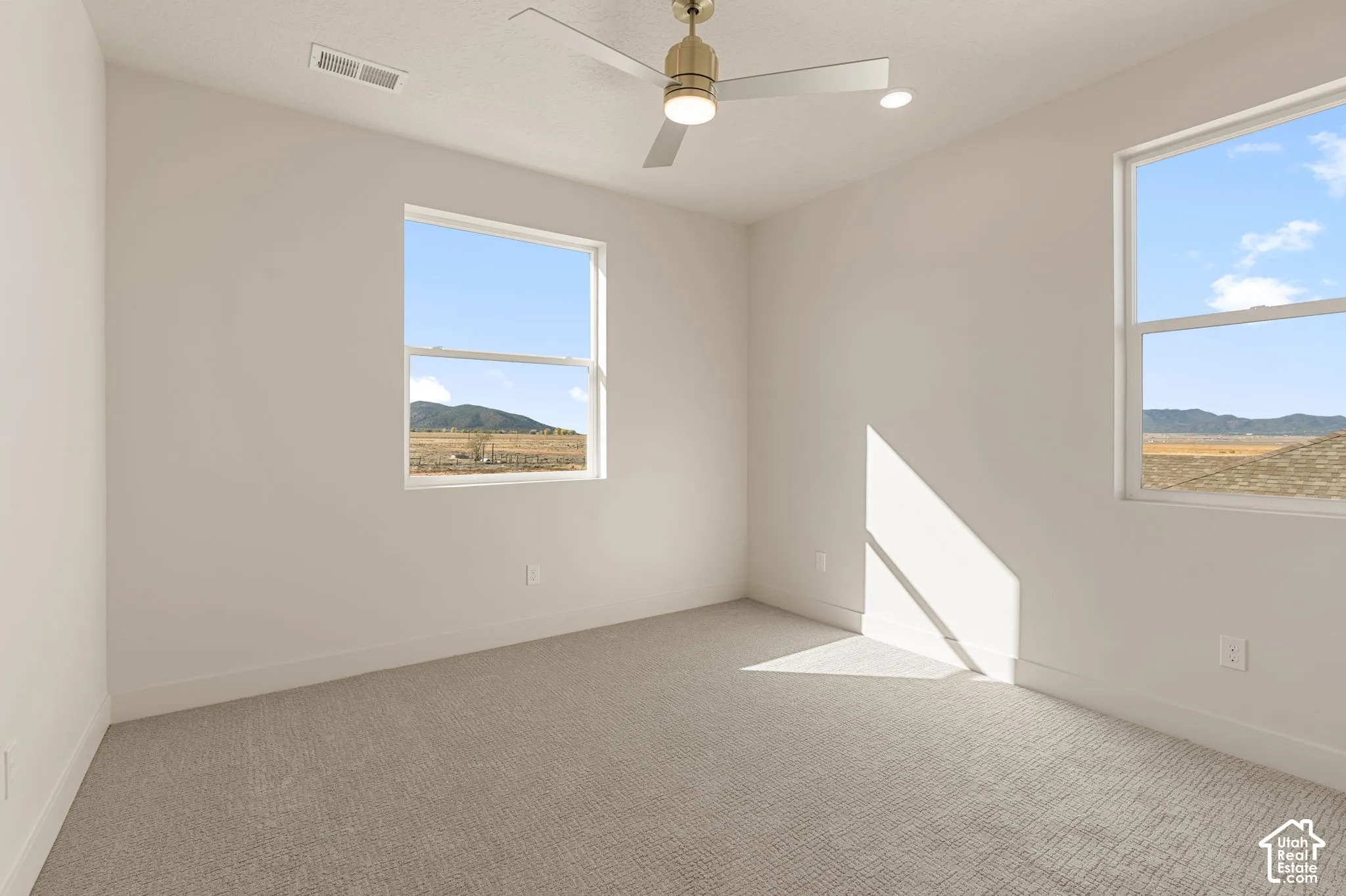 Neutral-toned interior featuring wall-to-wall carpeting, dual windows, a metallic finish ceiling fan with integrated lighting, and recessed ceiling lighting