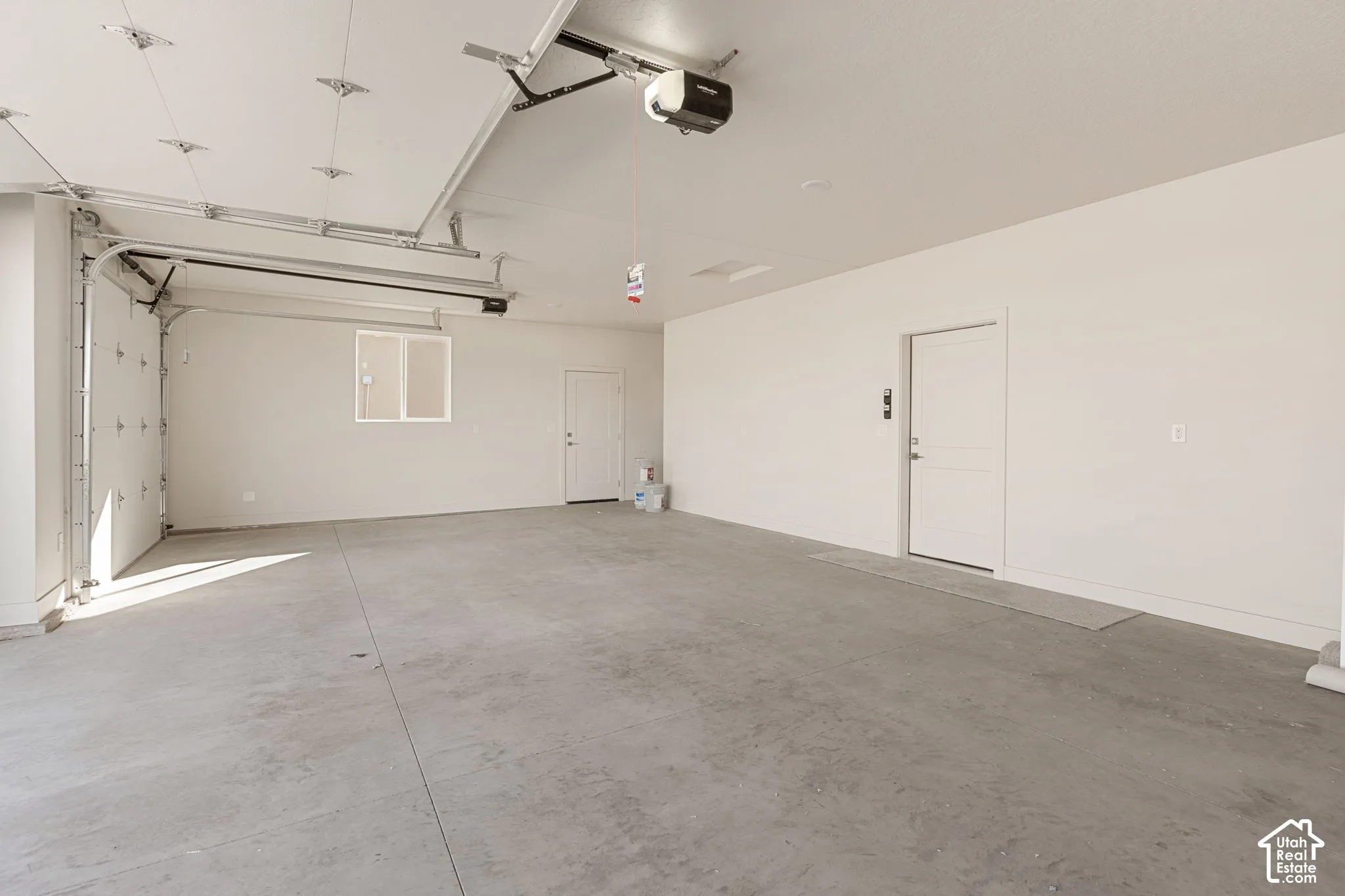 Spacious multi-car garage featuring a smooth concrete floor, finished interior walls, integrated ceiling-mounted door openers, and two separate door access points