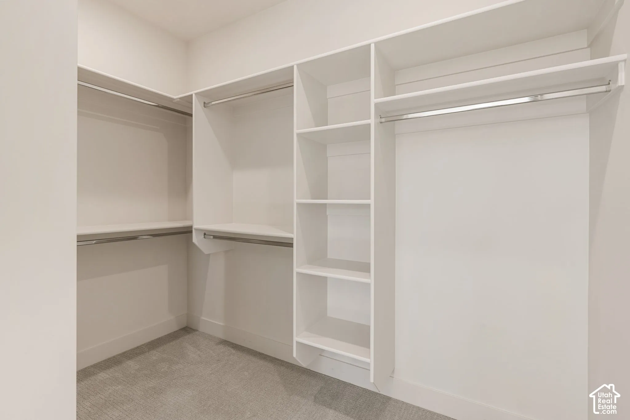 Walk-in closet featuring white built-in shelving, integrated vertical storage cubbies, and multiple metal hanging rods