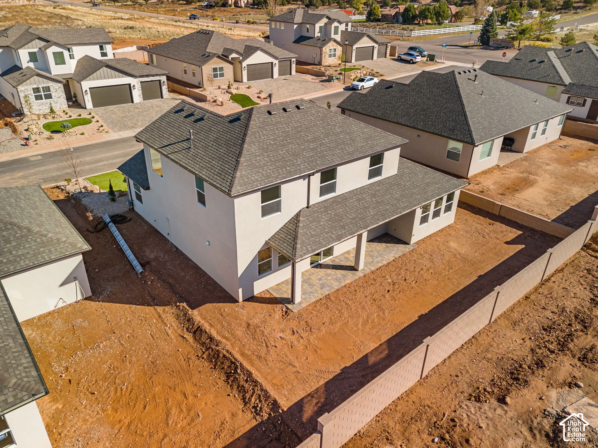 Two-story stucco exterior featuring a hip roof, covered rear patio with stone-finish pavers, and perimeter masonry wall