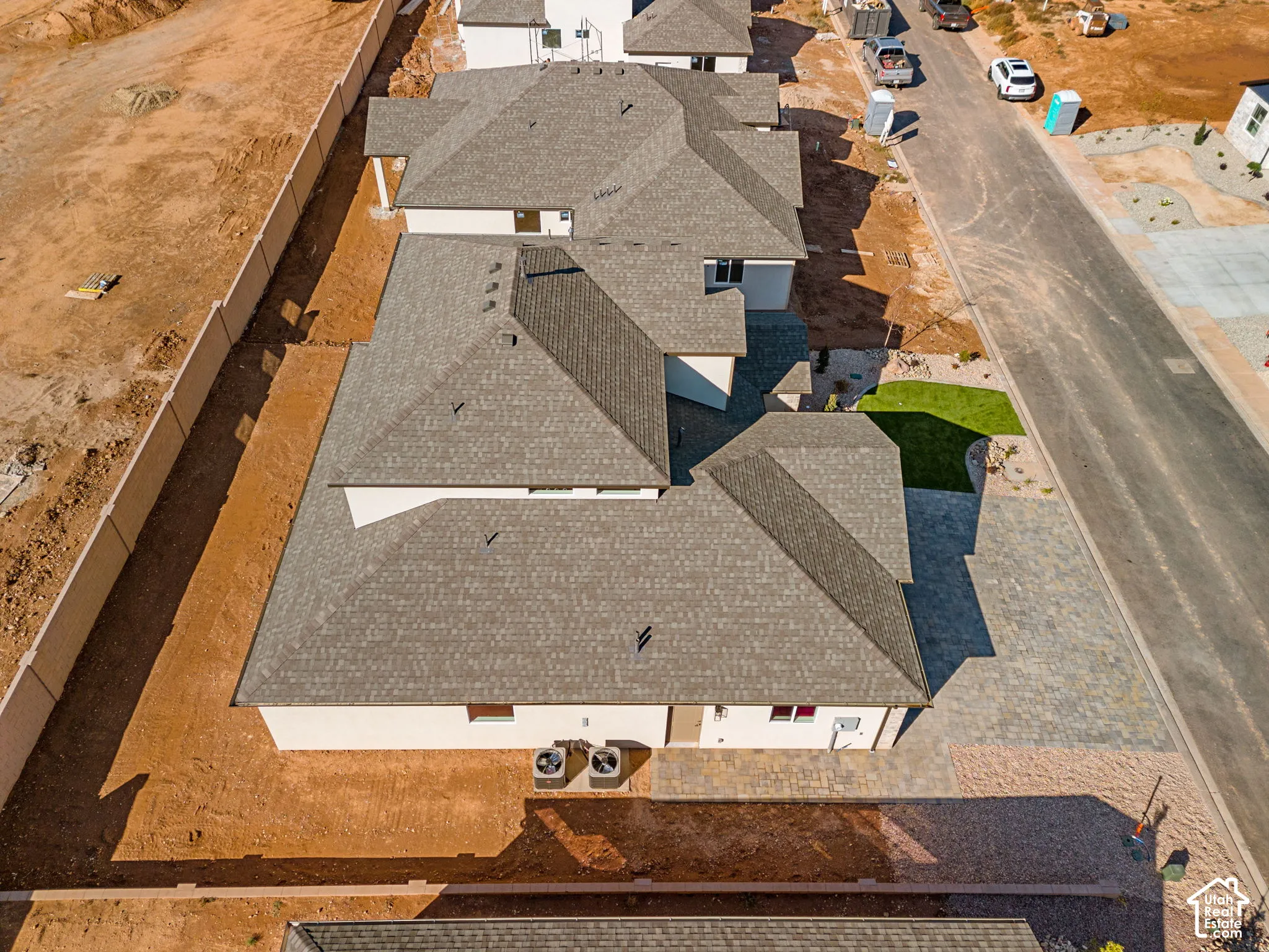 Aerial perspective of a single-story residence featuring a hipped roof, paved driveway, stone-paver entryway, and two exterior HVAC units