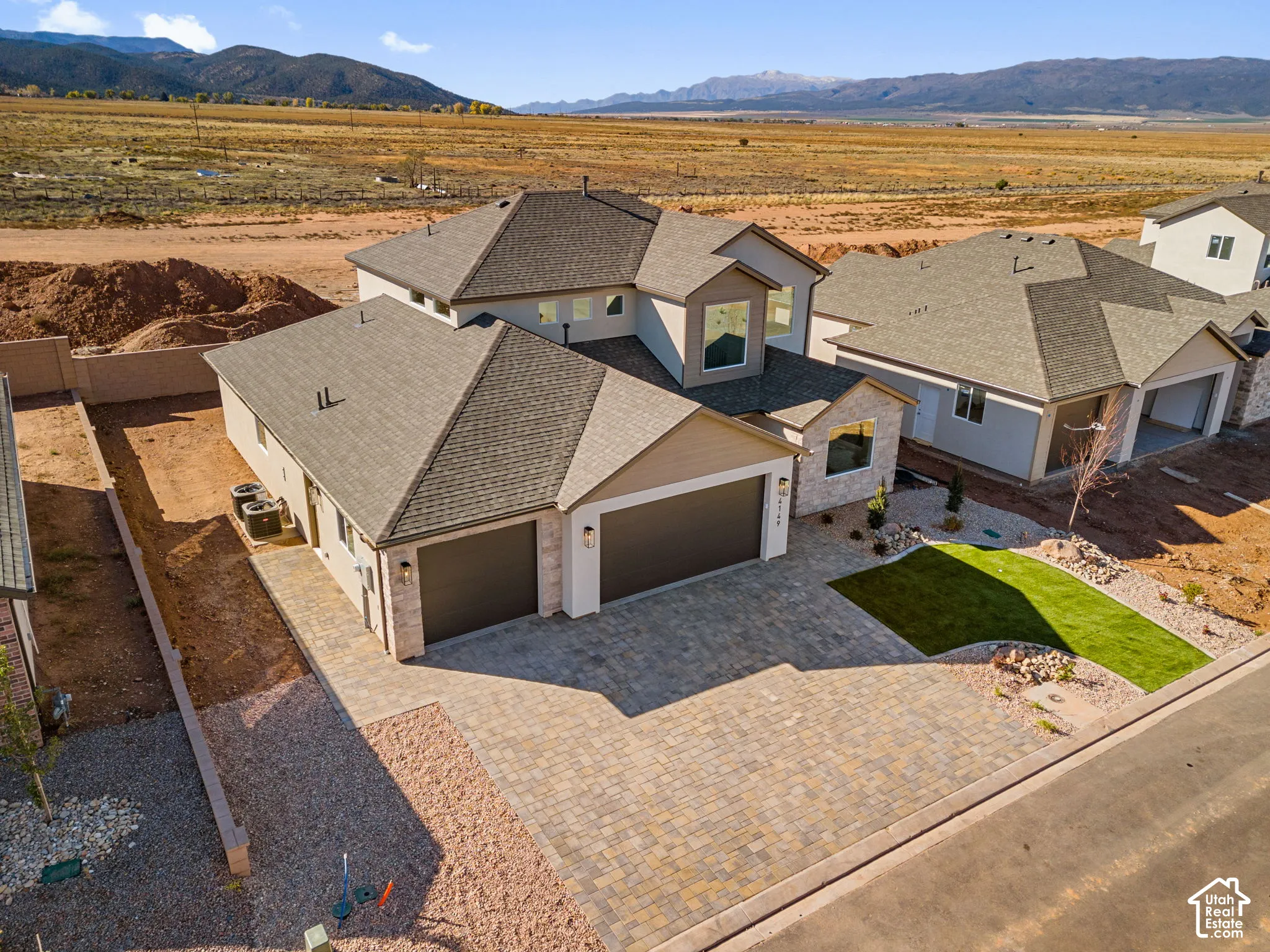 Two-story exterior featuring stone veneer accents, multi-faceted rooflines, a three-car garage, and a paver driveway set against a mountain backdrop