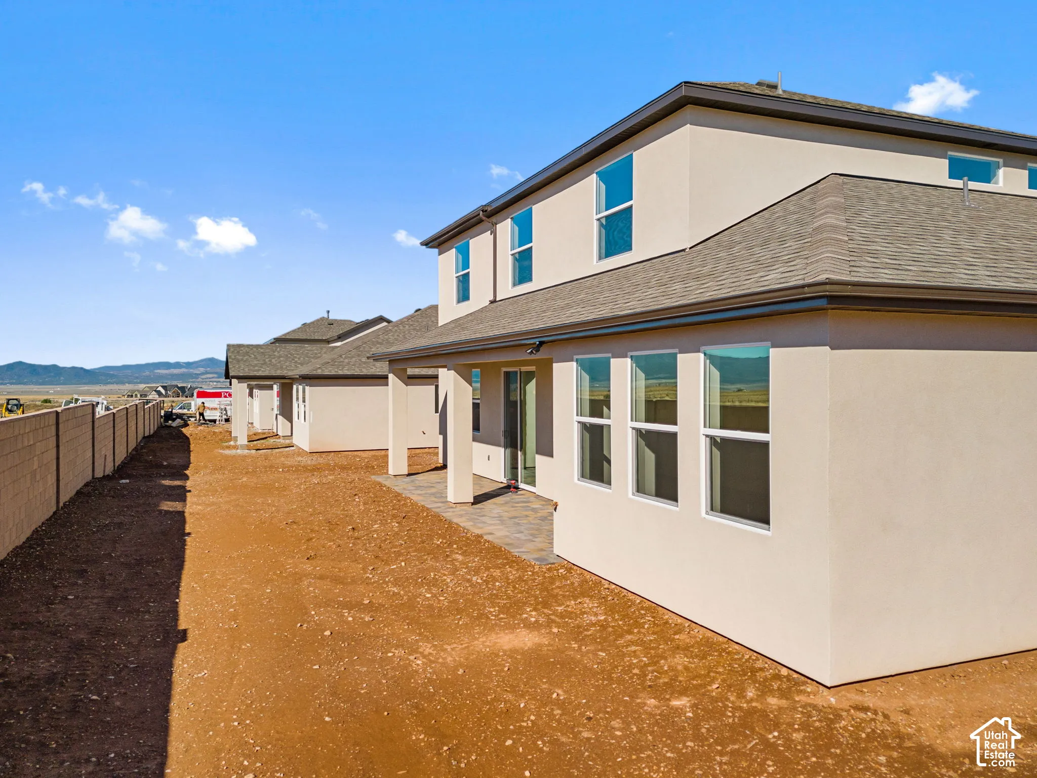 Two-story stucco exterior with a covered patio featuring paver flooring, multiple large windows, and a masonry perimeter wall