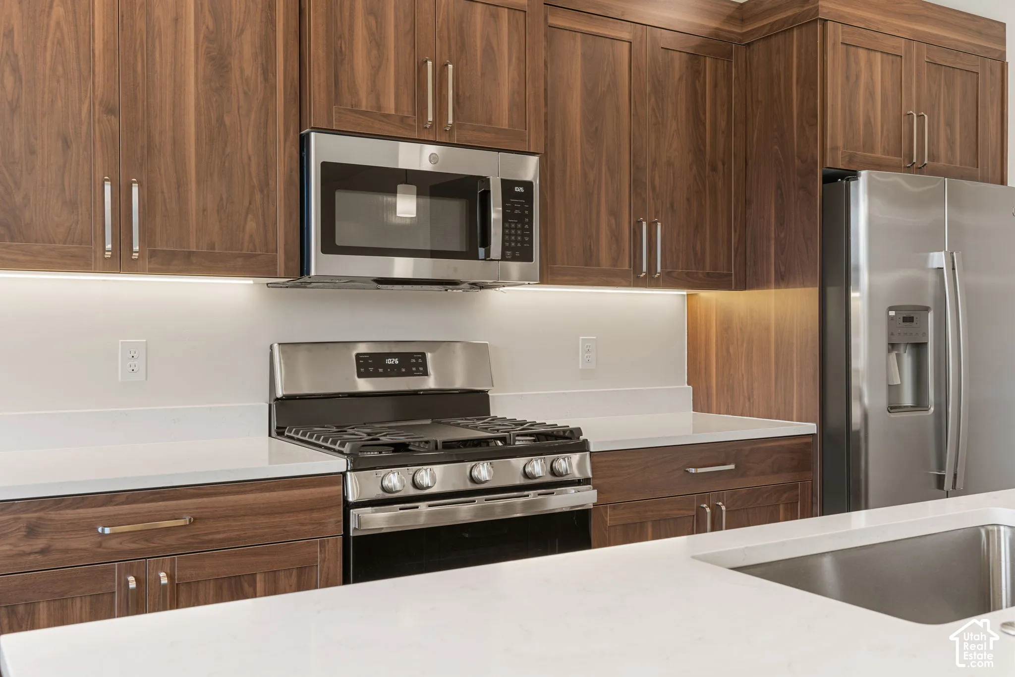 Kitchen featuring flat-panel wood-grain cabinetry, quartz countertops, stainless steel appliances, and under-cabinet lighting