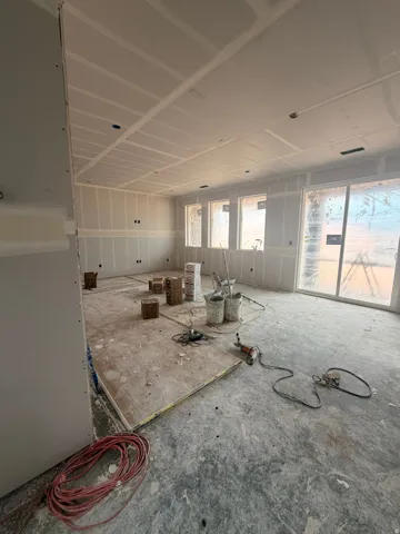 Expansive interior space featuring newly installed drywall, multiple windows for ample natural light, a sliding glass door providing exterior access, and recessed ceiling lighting