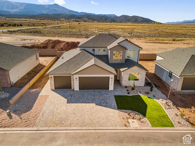 Two-story residence featuring a stone and siding exterior, multi-car garage, paver driveway, artificial turf lawn, and prominent mountain backdrop