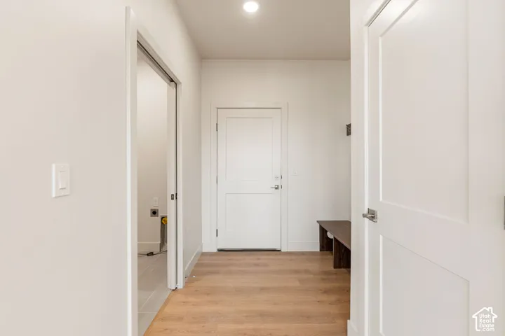 Neutral interior hallway featuring wood-finish flooring, two-panel shaker doors, recessed lighting, and a built-in wooden storage bench