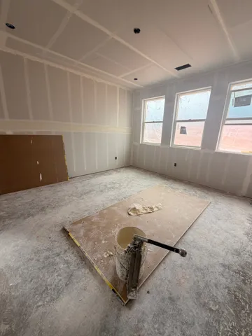Room with installed drywall, multiple windows, and a ceiling with recessed light fixtures