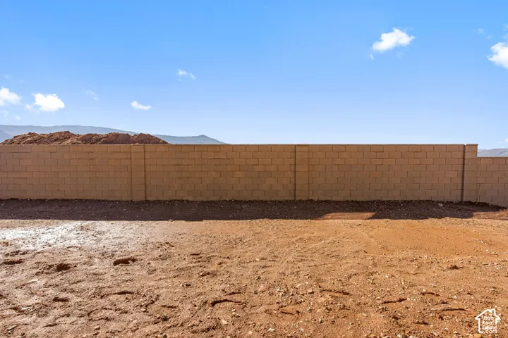 Expansive open lot featuring a concrete block perimeter wall and mountain scenery