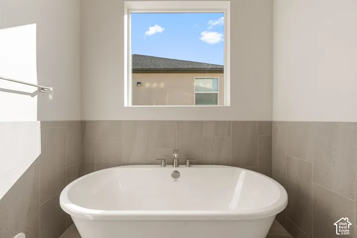 Freestanding soaking tub featuring a chrome faucet, set against tile wall surround and a square picture window