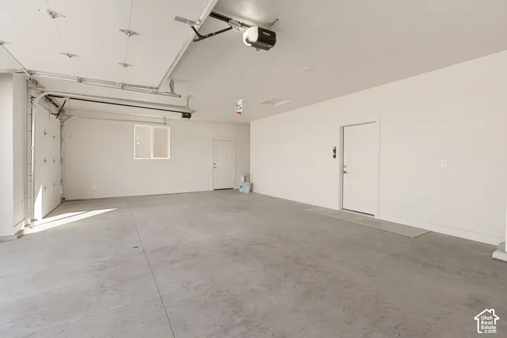 Spacious multi-car garage featuring a smooth concrete floor, finished interior walls, integrated ceiling-mounted door openers, and two separate door access points
