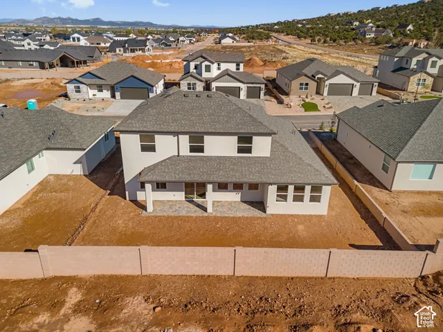 Two-story exterior featuring light-toned stucco siding, a multi-gabled asphalt shingle roof, a covered concrete patio, and a perimeter concrete masonry unit wall