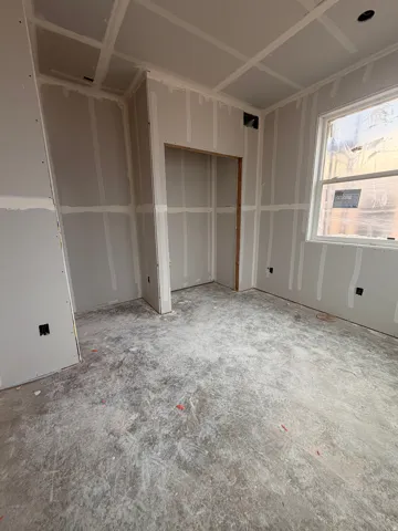 Room under construction featuring drywall installation, ceiling details, window opening, and a built-in alcove