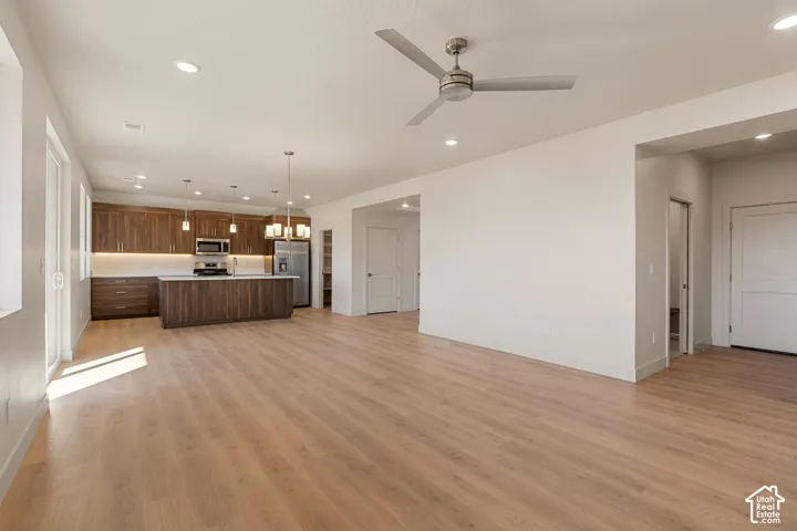 Open-concept interior featuring wood-finish flooring, recessed lighting, a modern ceiling fan, and a kitchen equipped with cabinetry, a central island, and stainless steel appliances