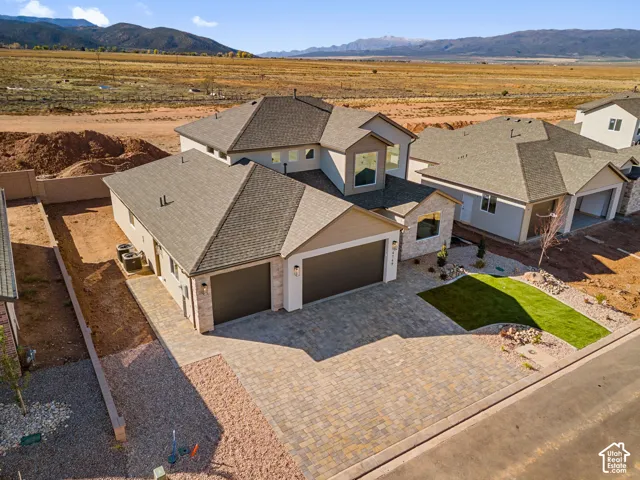 Two-story exterior featuring stone veneer accents, multi-faceted rooflines, a three-car garage, and a paver driveway set against a mountain backdrop