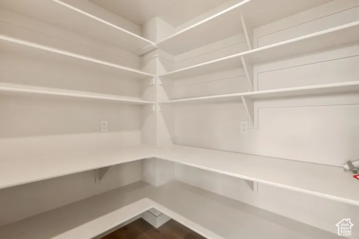 Walk-in storage area featuring white multi-level corner shelving, shiplap wall detailing, and wood-finish flooring