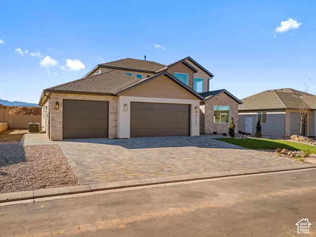 Multi-level exterior featuring a stone and horizontal siding facade, paver driveway, and a three-car garage