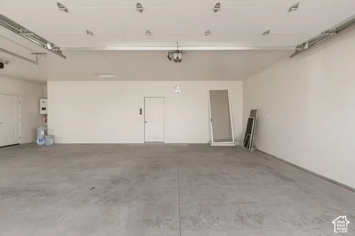 Finished garage featuring smooth concrete flooring, high ceilings with mounted lighting, crisp white wall finishes, and a dedicated wall-mounted tankless water heater