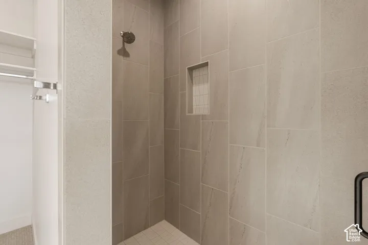 Walk-in shower featuring large-format neutral wall tile, mosaic tile shower floor, integrated tiled recessed niche, and a wall-mounted chrome shower head
